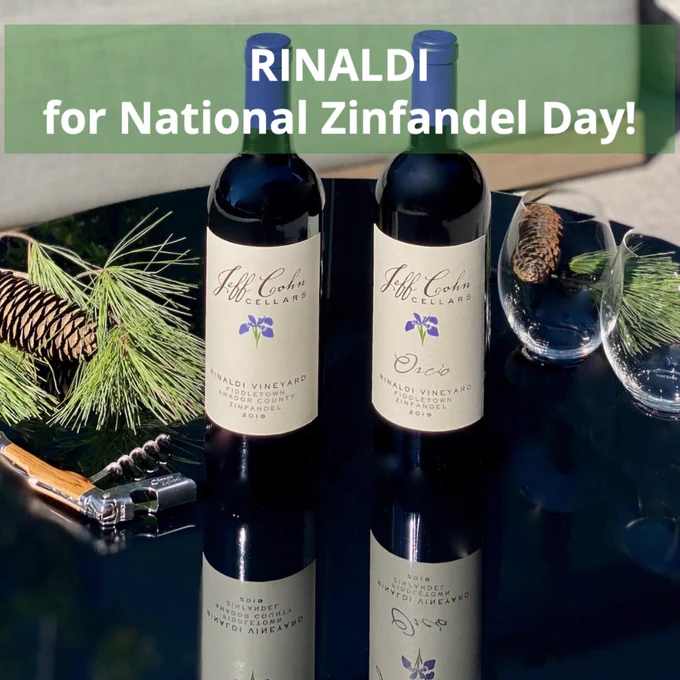 Bottles of Jeff Cohn Cellars 2019 Rinaldi and Orcio Zinfandel on a table with glasses and pine branches on a black glass table.