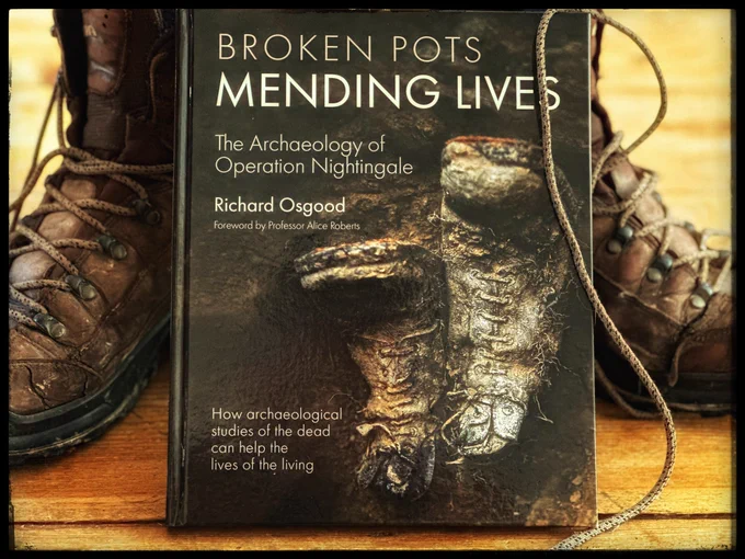 Two digging boots behind the book ‘Broken Pots, Mending lives’