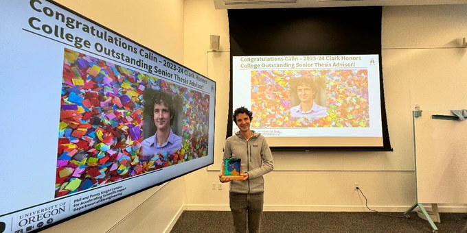 A man holds up an award while standing in front of two screens