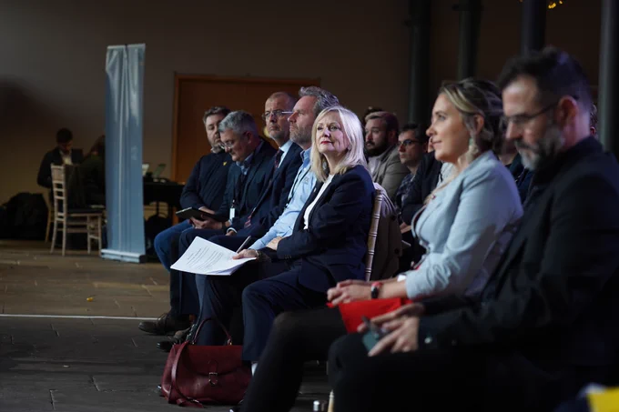 An audience are sat watching speakers at the West Yorkshire Innovation Festival. Tracy Brabin is sat in the middle of the crowd.