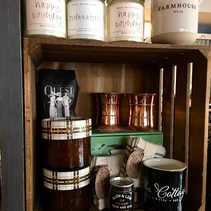 A stack of gifts, including candles and mugs, in a wood crate.
