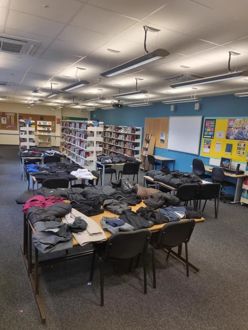 Photo of the school library, with all 5 tables covered in jumpers, jackets etc.