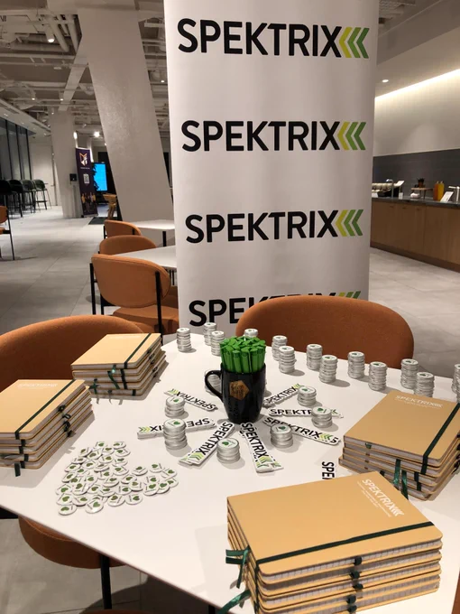 Spektrix notebooks, stickers, pens and lip balms arranged on a table in front of a Spektrix banner