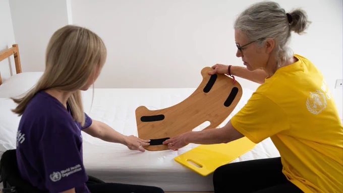 A person in a wheelchair with a health worker showing the bottom of a curve shaped transfer which has a grip surface.