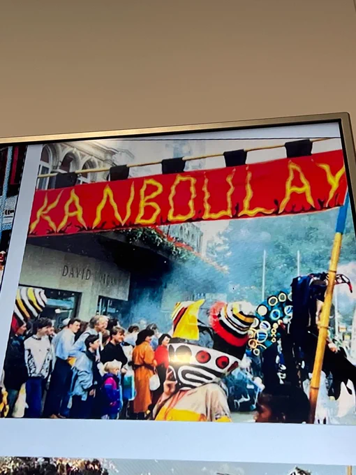 An image taken from Canboulay - a precursor to the Trinidad and Tobago Carnival. At the top is a red banner with Kanboulay written in yellow. At the bottom, a group of people in carnival mask and costume dance and celebrate.