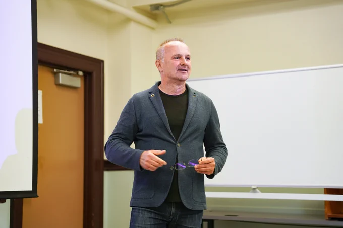 SOJC professor of practice Atilla Schillinger stands at the front of a classroom.