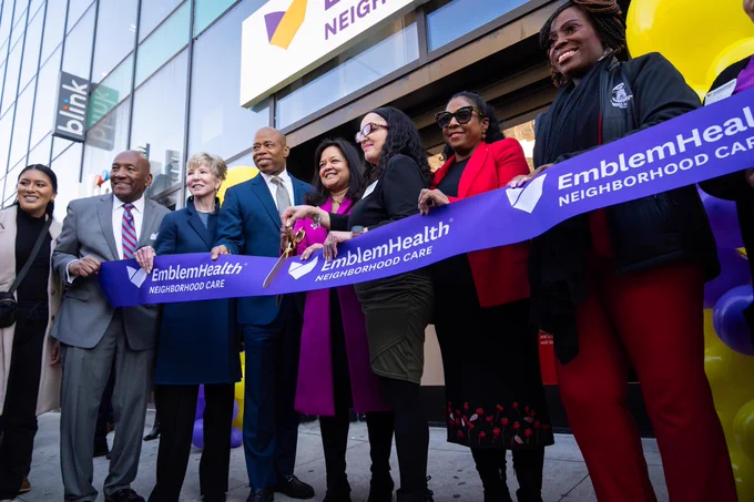 mayor and other city officials and community leaders hold big purple ribbon with scissors in front and building behind them