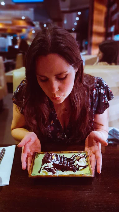 photo of turtletickles looking down and blowing out a tiny yellow candle on a slide of chocolate fudge cake 