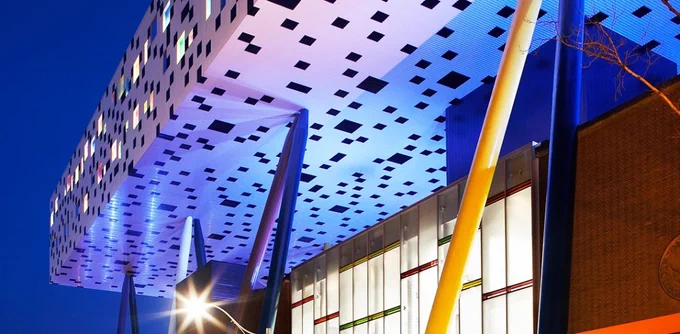 A photograph of OCAD campus at night. The trademark black and white pixelated building is lit from within and below.
