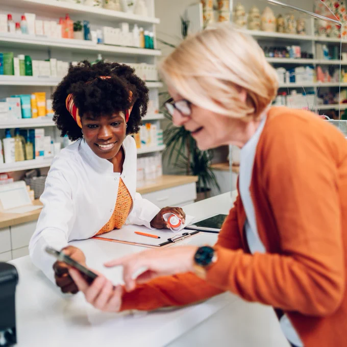 An image of  woman showing a prescription on a smartphone to a pharmacist. 