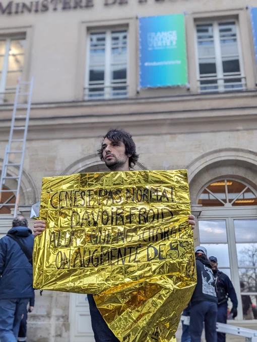 Un militant écologiste tient une pancarte devant le Ministère de l'économie, sur laquelle est écrit "C'est pas normal d'avoir froid alors que nos charges ont augmenté de 5 euros"