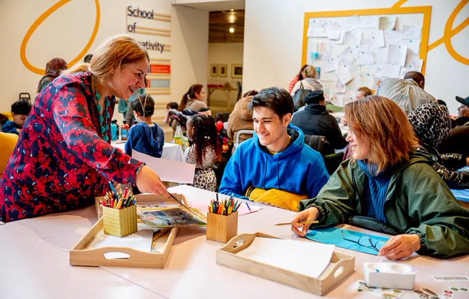 Three people sat at table in conversation. One person is holding the drawing in her hands while the other two are looking at it and smiling. Image courtesy of Shirlaine Forrest