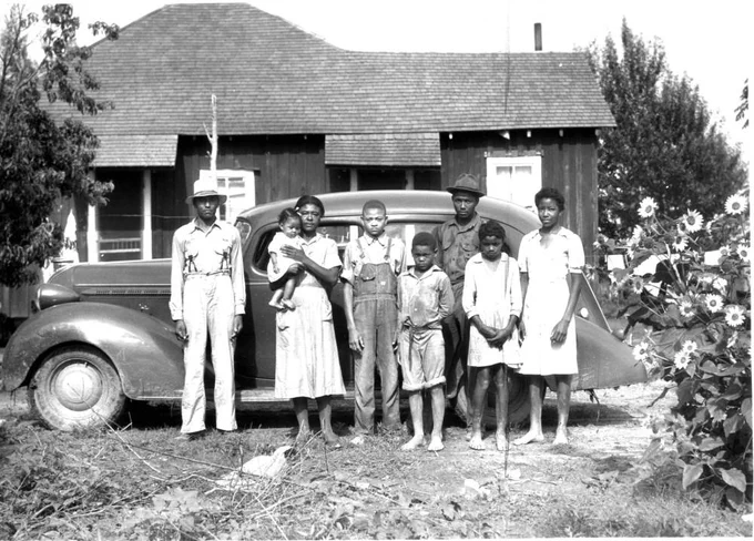 Black and white photo of African American family standing by vehicle in front of house