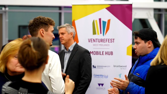 An image of two delegates talking at the Venturefest West Midlands Mobile Hub amongst a crowd of additional attendees.