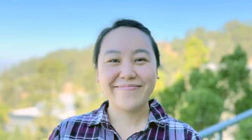 Smiling woman with sunny hillside in background.