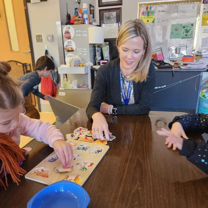 A female substitute teacher working at a table with students.