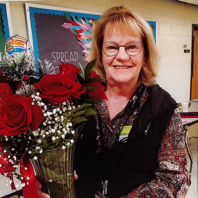 A female substitute teacher holding flowers and smiling for the camera.