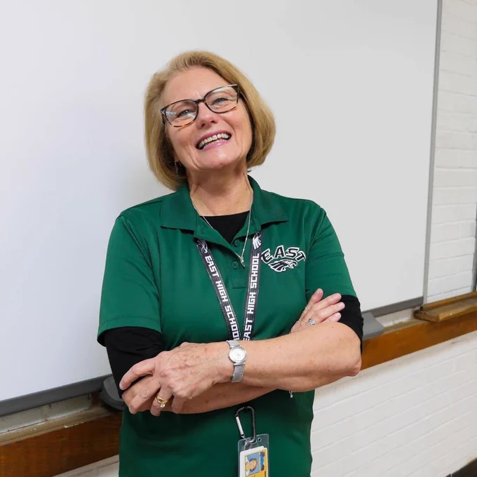 A female substitute smiling with her arms folded in a classroom.