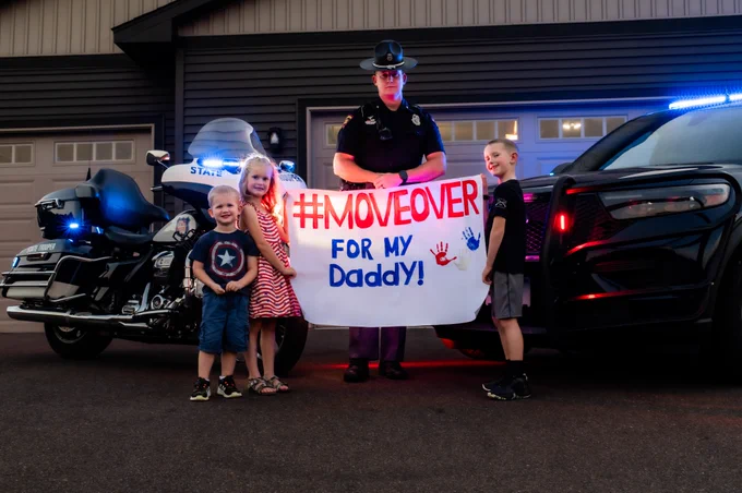 Children hold sign that reads: Move over for my daddy, standing in front of trooper and State Patrol vehicles.