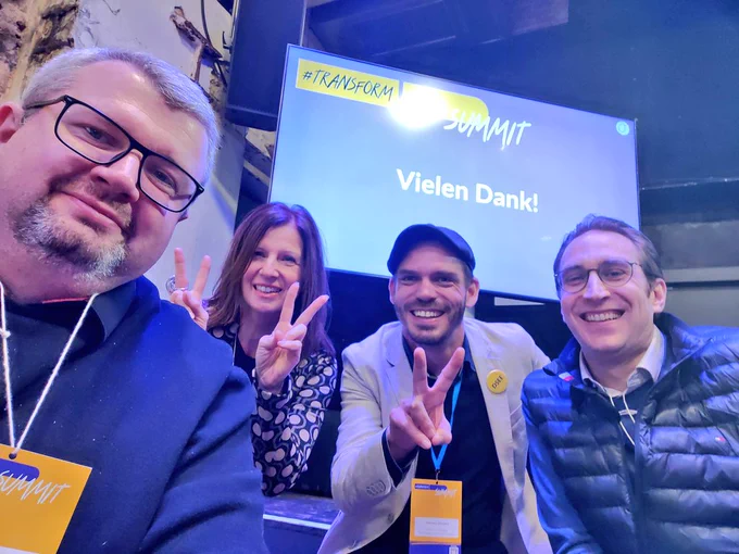 Gruppen-Selfi mit David, Andreas, Sabine und Hannes - im Hintergrund ein Monitor, auf dem "Vielen Dank!" zu lesen ist.