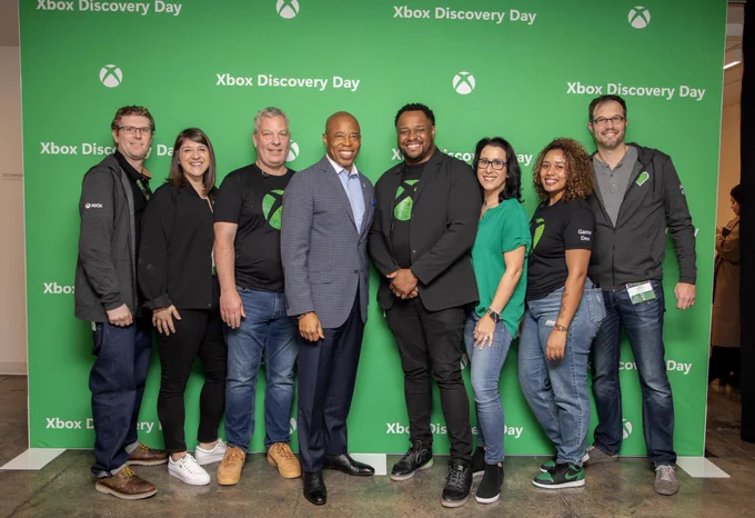 Mayor Adams stands with tech leaders and game leaders in front of a green backdrop