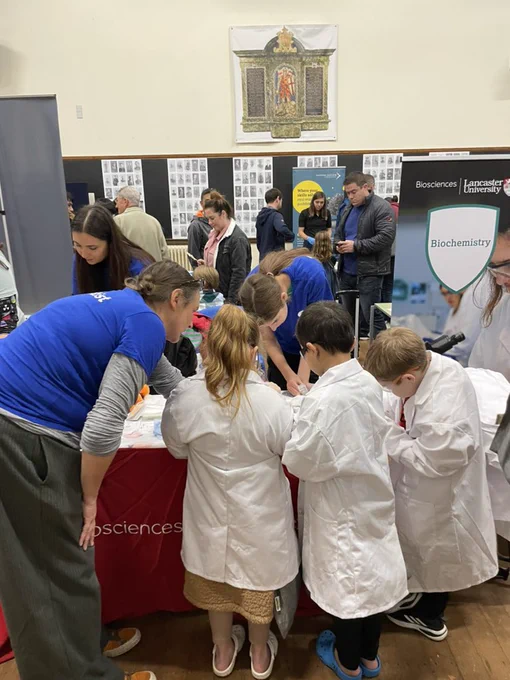 Dr Sarah Allinson helps children wearing lab coats to extract DNA from strawberries