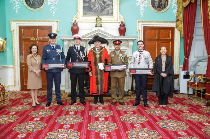 Lord Mayor stood in the centre wearing his scarlet Alderman's gown with 2 aide-de-camps wither side of him each wearing uniform and holding their freedom certificates. On the far left the lady mayoress wearing a beige dress and on the right the deputy clerk of the chamberlain's court wearing a black legal gown. 