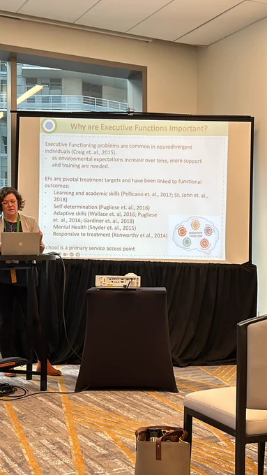 Dr. Laura Anthony presenting at a podium in front of projector screen.