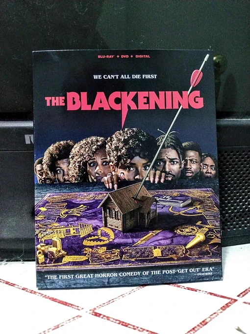 Blu-ray of the blackening shows 7 black people peering over a game board.  A cabin is at the center of the board with an arrow sticking out if it.  The tag line reads, We can’t all die first.   Further text reads, "THE FIRST GREAT HORROR COMEDY OF THE POST GET OUT ERA" - Indie wire.