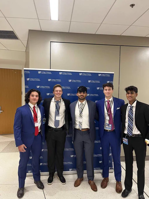 Five male students smile while standing in front of a blue backdrop with the U-F College of Medicine logo.