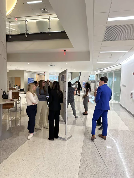 Three groups of students stand in front of research posters while discussing their work. 