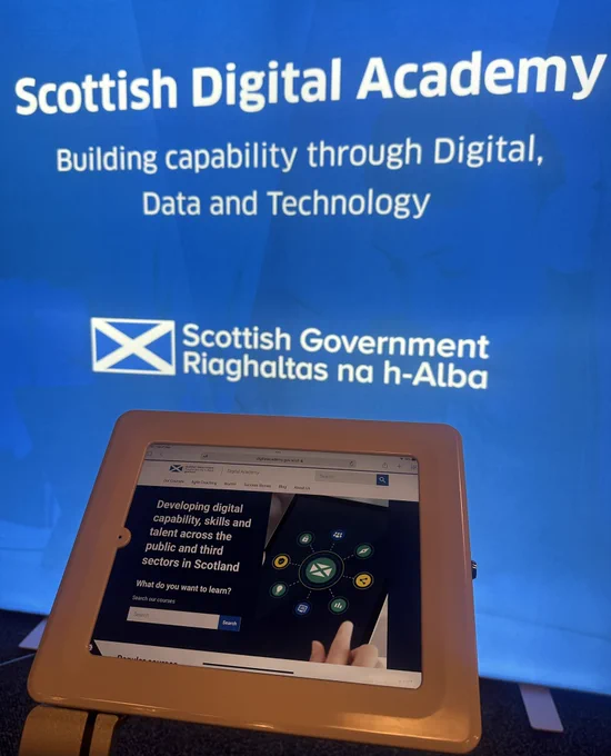 A blue light box with white writing saying Scottish Digital Academy with the Government logo and an old displaying the website.