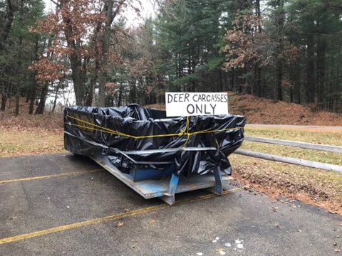 A dumpster, lined with black plastic, bearing a sign that reads "Deer Carcasses Only."