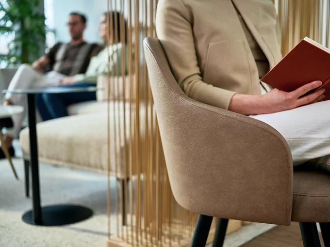 A woman reads a book in a modern healthcare waiting room with Steelcase Health West Elm Collection workplace furniture. 