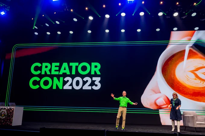 ServiceNow employee, Chuck, stands alongside presenter Lauren on a large keynote stage. He is wearing a bright green shirt and a bowtie. Behind them a sign reads CreatorCon 2023.
