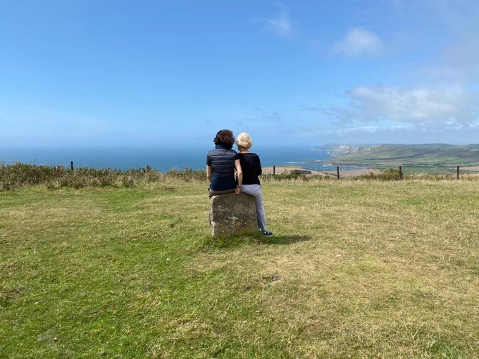 My mum and me from the back, sitting on a mile stone and looking at the sea and the sky