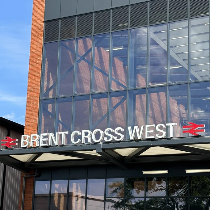 Front view of the brand new station, 'Brent Cross West' which features large, modern glass windows, the station name in bold white letters and red National Rail logo's either side.