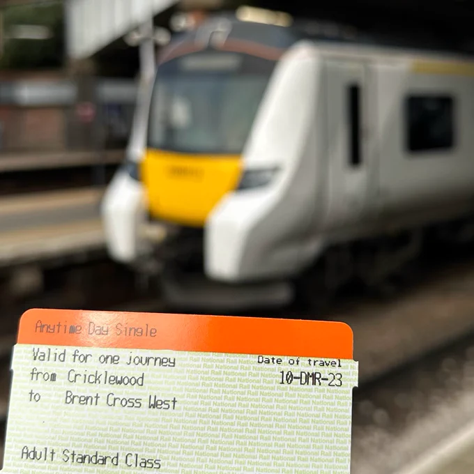 An orange and white train ticket which reads "Valid for one journey from Cricklewood to Brent Cross West", with a blurred Thameslink train in the background.