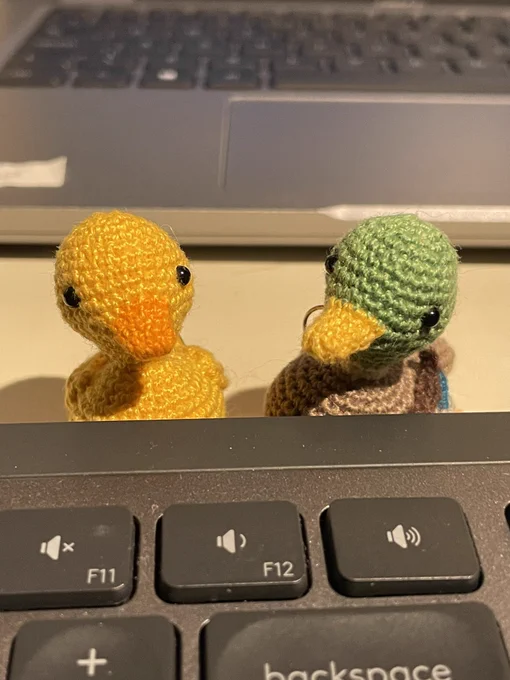 Two mini crochet ducks sitting behind a computer keyboard.