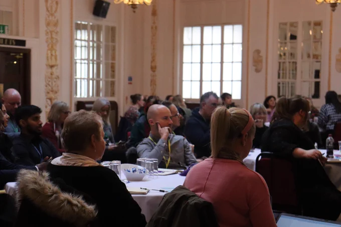 This is an image of attendees sitting around tables facing a stage. 