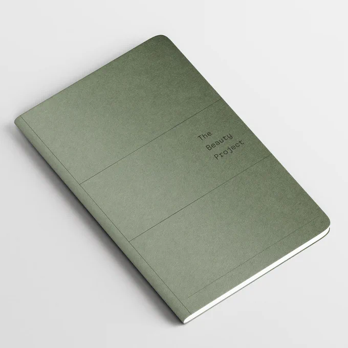 A green 'The Beauty Project' lab book on a white background