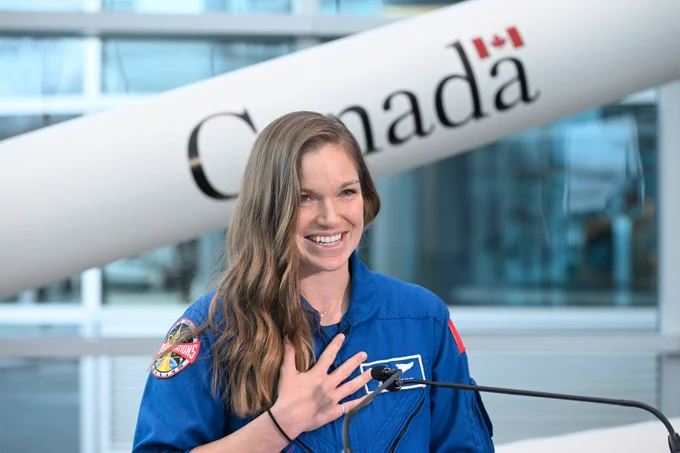 Astronaut woman smiling, with her hand rested on her upper chest.