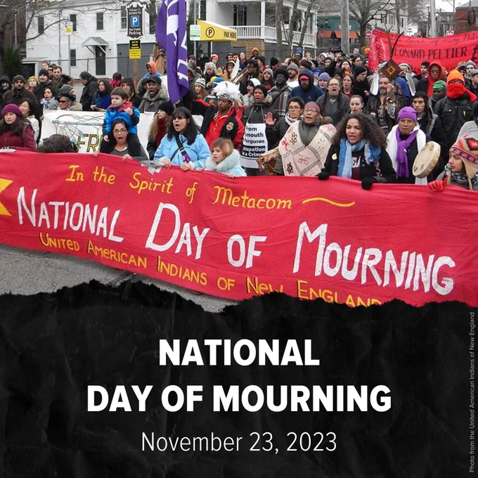 Crowd of marchers with big red sign that says, "In the Spirit of Metacom, National Day of Mourning, United American Indians of New England." Below photo, text says, "National Day of Mourning. November 23, 2023." Crowd of marchers with big red sign that says, "In the Spirit of Metacom, National Day of Mourning, United American Indians of New England." Below photo, text says, "National Day of Mourning. November 23, 2023." Photo from United American Indians of New England.
