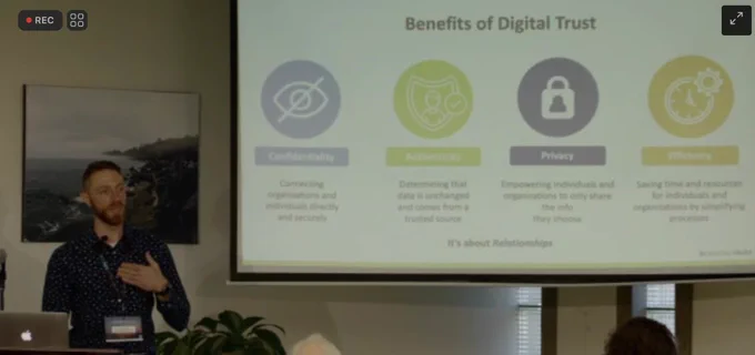 Photo of presentation in front of a slide reading “Benefits of Digital Trust”