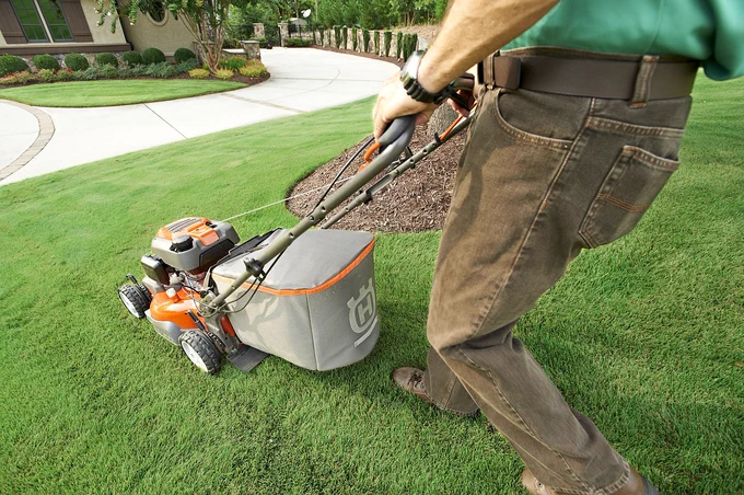 A man cuts the grass in a garden with a lawn mower.