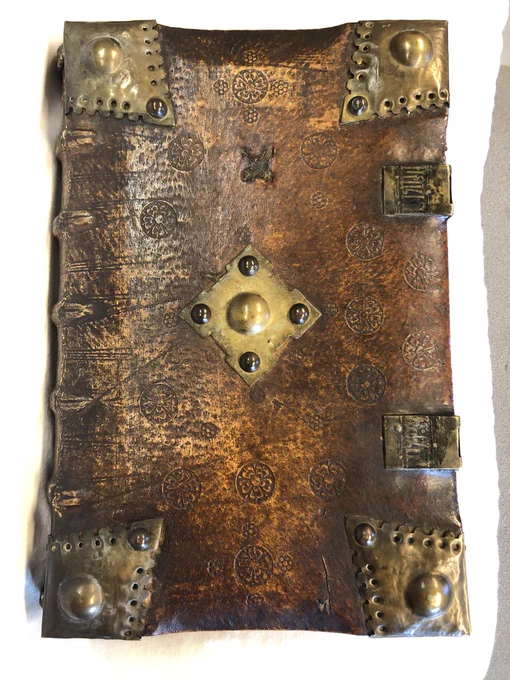 Image of book from brown leather front cover with metal furniture on all four corners and one in the centre. Two metal clasps on right edge of book.