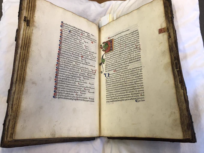 Image of the book open. Left side shows capital spaces with red and blue and right hand side has illuminated initial showing stylized D in red, blue and gold. 