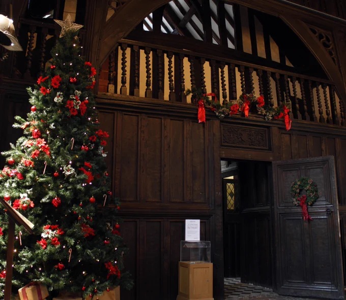 A photo showing The Commandery's Great Hall decorated for Christmas; a Christmas tree stands on the left and a wreath is hanging on the door.