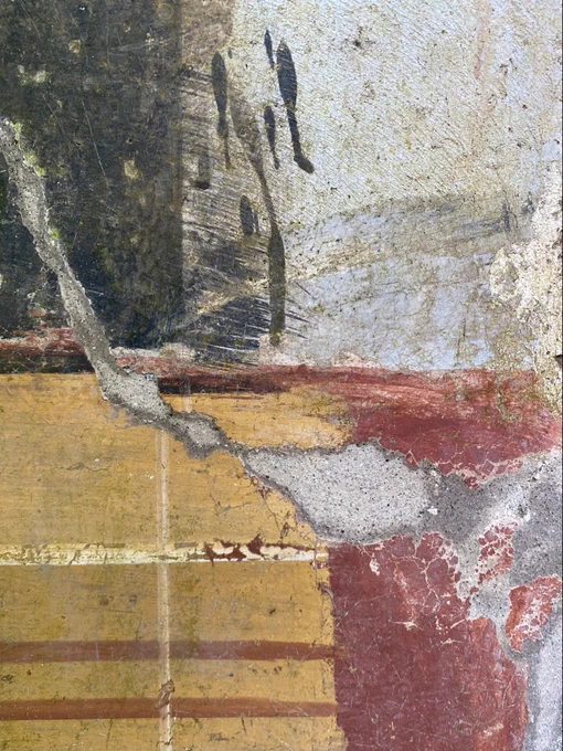 A close up detail of the unfinished fresco: the black background gives way to a white border onto which at the bottom have been carelessly dripped some black paint. The yellow border ends roughly awaiting the painting of the more formal border, presumably matching the red and green one on the other side.