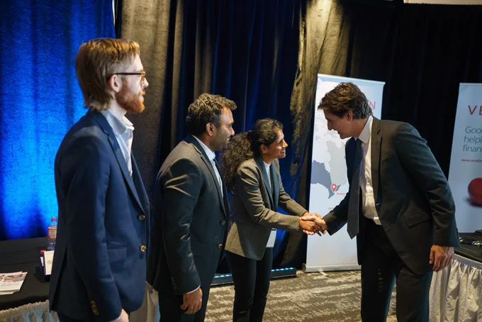 Prime Minister Justin Trudeau is standing and shaking hands with a woman, who is standing in front of him. Both of them are smiling. Two men are standing beside the woman.